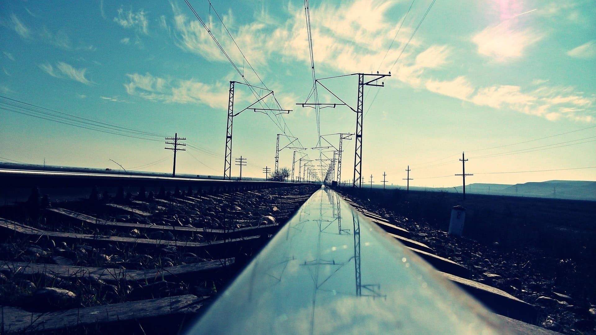 A railway track shot at rail level, running to the horizon between overhead line poles